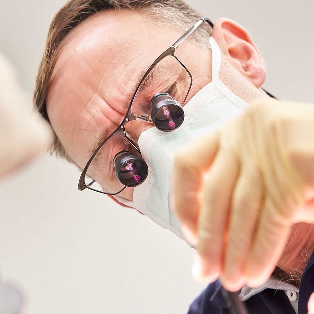Zahnarzt Jochen Holz mit Mikroskopbrille bei der Behandlung in der Zahnarztpraxis Wetzlar, von unten fotografiert.