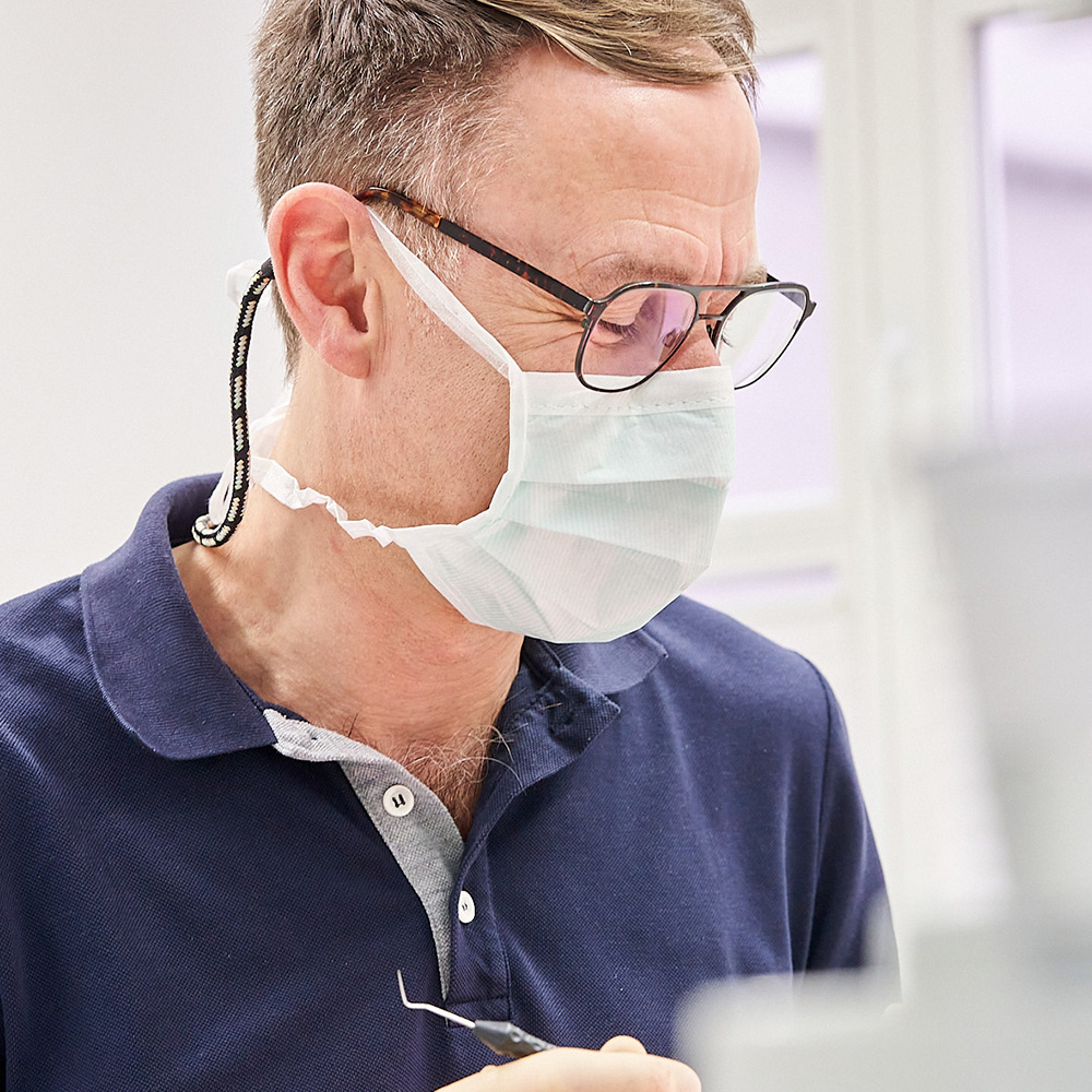 Zahnarzt Jochen Holz mit Brille und Maske lächelt bei der Behandlung.